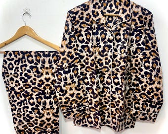 Puede incluir: Un conjunto de pijama de dos piezas con estampado de leopardo en negro, marrón y crema. La parte superior de manga larga tiene cuello y cierre de botones. Los pantalones son largos y tienen un estampado a juego. Ambas piezas tienen ribete blanco.
