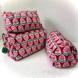 May include: Three quilted fabric pouches featuring a repeating floral pattern in shades of deep red, light pink, and teal. Each rectangular bag includes a white zipper closure, and one pouch displays a decorative green tassel attached to the side.