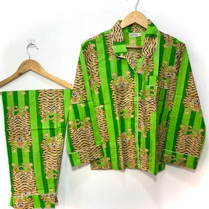 May include: Green striped pajama set with a tiger print. The set includes a button-down shirt with a chest pocket and pants. The pajamas have white trim and are hanging on a wooden hanger.