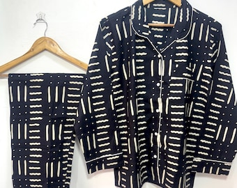 May include: Black pajama set with a white abstract pattern. The set includes a button-down shirt with a chest pocket and long pants. The shirt and pants are hanging on wooden hangers against a white background.