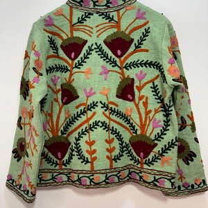 May include: A light green jacket with intricate floral embroidery. The jacket features a high collar and is adorned with brown, orange, pink, and burgundy floral patterns. The embroidery creates a textured, detailed design, perfect for a unique fashion statement.