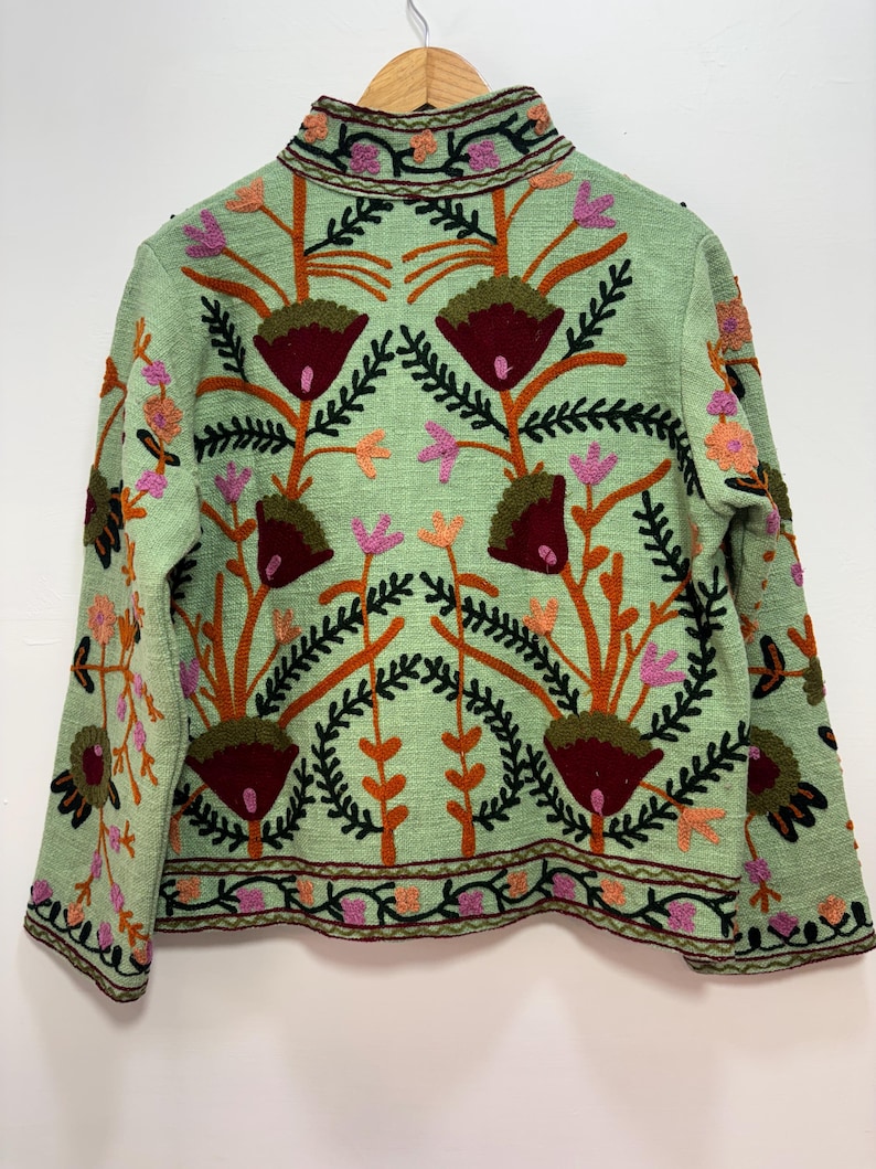 May include: A light green jacket with intricate floral embroidery. The jacket features a high collar and is adorned with brown, orange, pink, and burgundy floral patterns. The embroidery creates a textured, detailed design, perfect for a unique fashion statement.