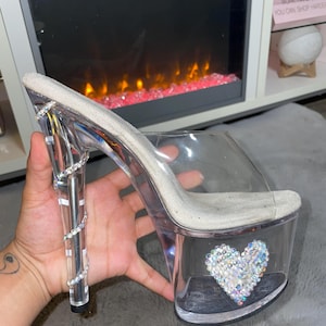 Könnte beinhalten: Transparente High-Heel-Plattform-Sandalen mit einem mit Strass besetzten Absatz und einem großen Strass-Herz auf der Plattform.