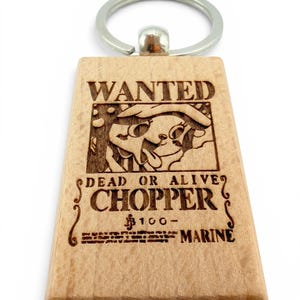 Può includere: Portachiavi in legno con un'etichetta rettangolare con l'immagine incisa di Chopper di One Piece. L'etichetta recita "WANTED" e "DEAD OR ALIVE CHOPPER" con una taglia di 100 Marine. Ha un anello di metallo argentato.
