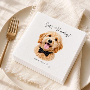 Op de afbeelding: Een wit vierkant papieren servet met een gedrukte illustratie van een goudkleurige hond met een zwarte vlinderdas. De tekst Let's Pawty! staat boven de hond en de tekst LOVE LUCY met twee kleine pootafdrukken staat eronder.