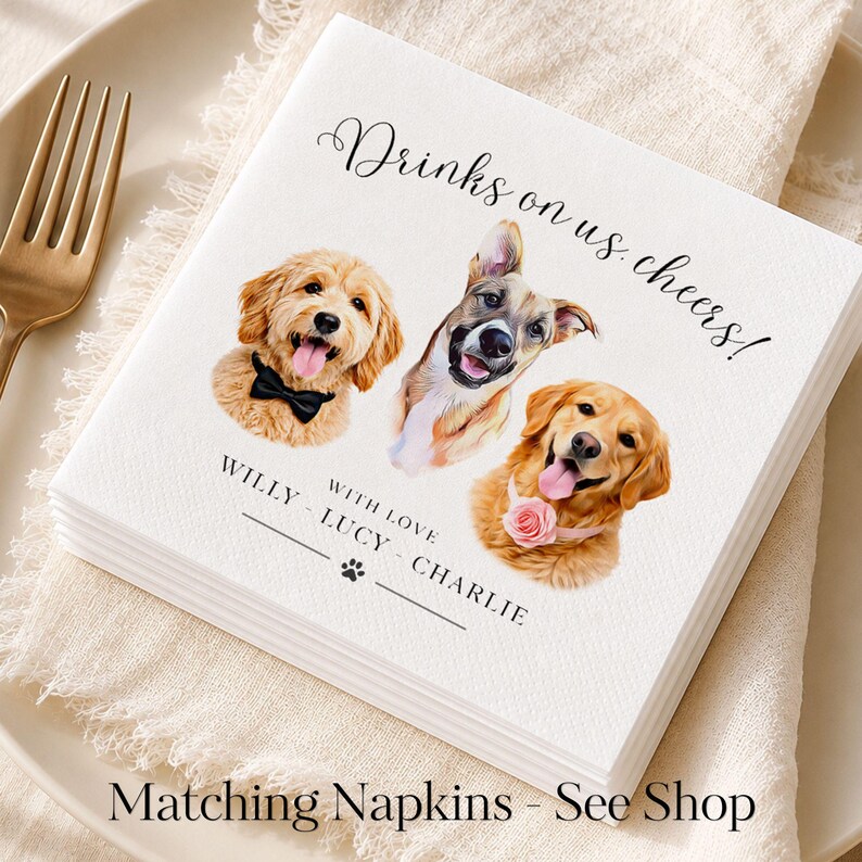 May include: A white square paper napkin featuring the printed text Drinks on us, cheers! and WITH LOVE WILLY - LUCY - CHARLIE with a paw print. The design includes three illustrated dog portraits: one wearing a black bow tie, one plain, and one with a pink flower collar.