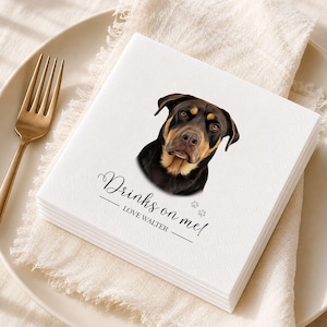 Op de afbeelding: Een vierkant wit papieren servet met een realistische illustratie van een zwart-bruine hond. De tekst "Drinks on me!" staat boven de naam "LOVE WALTER" en twee kleine grijze pootafdrukken op een bord met een vork.