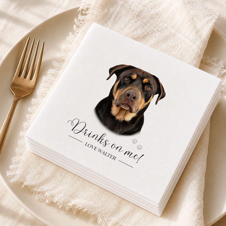 Op de afbeelding: Een vierkant wit papieren servet met een realistische illustratie van een zwart-bruine hond. De tekst "Drinks on me!" staat boven de naam "LOVE WALTER" en twee kleine grijze pootafdrukken op een bord met een vork.