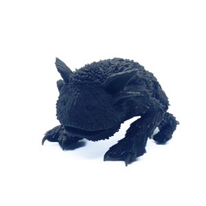 Puede incluir: Una criatura negra, impresa en 3D, peluda con una boca ancha y garras afiladas. La criatura está en posición de cuclillas, como si estuviera a punto de abalanzarse.