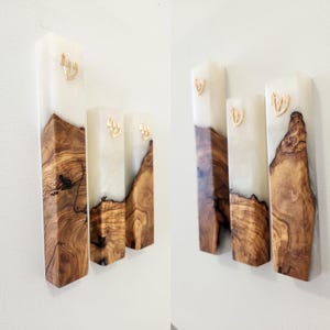 May include: Three rectangular mezuzah cases featuring a combination of natural brown wood grain and translucent white resin. Each piece is vertically oriented and displays a small, gold-colored Hebrew letter Shin mounted on the upper resin section.