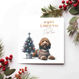 Può includere: Biglietto di Natale con un cane marrone con un maglione, accanto a un albero di Natale decorato. La carta ha un testo dorato che recita "Buon Natale alla migliore mamma di cane". L'immagine è incorniciata da un fogliame festivo.