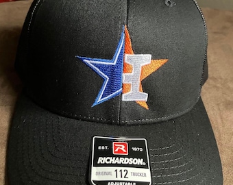 May include: A black trucker hat featuring an embroidered star logo split between blue and orange, with a white letter H in the center. A black and white sticker on the brim reads EST. 1970 RICHARDSON ORIGINAL 112 TRUCKER ADJUSTABLE.