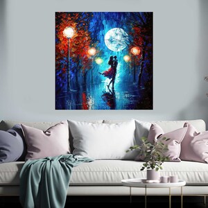 May include: A square canvas painting depicts a couple dancing in the rain under a full moon. The artwork features vibrant colors, with a focus on blues, reds, and oranges. The painting is displayed above a white sofa with pink and blue pillows.
