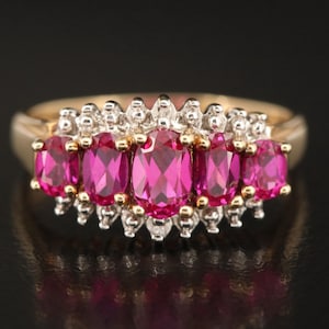 May include: A gold ring with a row of five oval-shaped pink gemstones surrounded by smaller white gemstones.