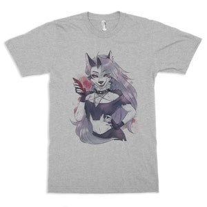 May include: A light gray t-shirt featuring a cartoon illustration of a wolf-like character with long gray hair, holding a red phone. The character is wearing a black choker and a black top. Red accents are visible in the background.