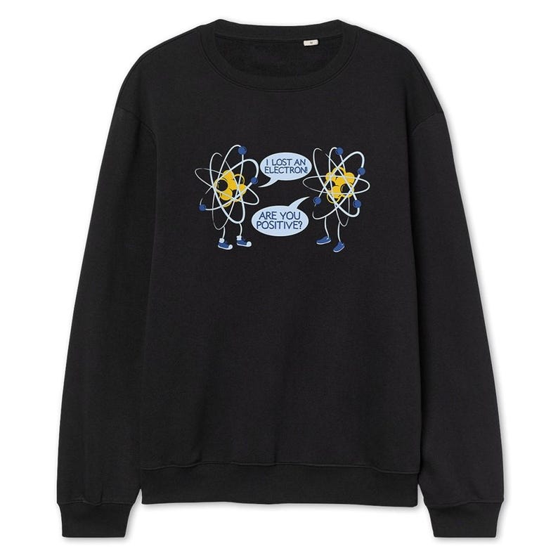 May include: Black sweatshirt featuring a humorous graphic of two cartoon atoms with speech bubbles. One atom says, "I lost an electron," and the other replies, "Are you positive?" The atoms are yellow with white and black details.