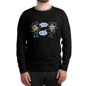 May include: Black sweatshirt featuring a humorous cartoon design of two atoms with legs and arms. One atom says, "I lost an electron," and the other replies, "Are you positive?" The design is in white and yellow.