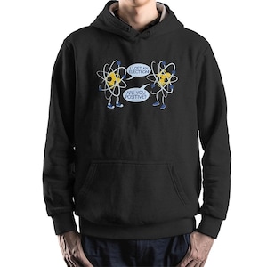 May include: Black hooded sweatshirt with a front pocket. The graphic features two cartoon atoms with the text "I lost an electron" and "Are you positive?" in speech bubbles. The atoms are yellow, white, and blue.