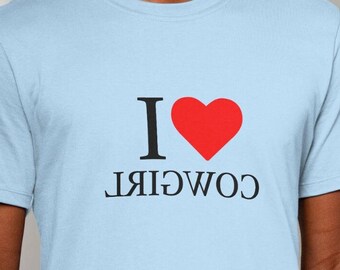 Könnte beinhalten: Ein hellblaues T-Shirt mit einem roten Herzen und dem Text "I COWGIRL" auf der Vorderseite.