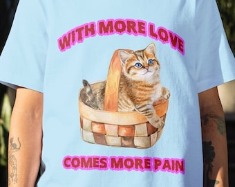 May include: A light blue t-shirt with a graphic of a cat sitting in a basket. The text "WITH MORE LOVE COMES MORE PAIN" is printed in pink on the shirt.