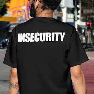 Op de afbeelding: Een zwart T-shirt met het woord "INSECURITY" in wit op de rug.