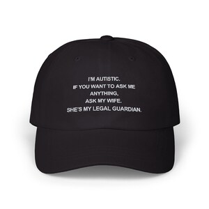 May include: Black baseball cap with white text: "I'M AUTISTIC. IF YOU WANT TO ASK ME ANYTHING, ASK MY WIFE. SHE'S MY LEGAL GUARDIAN." The cap has a curved brim and a fabric strap closure.