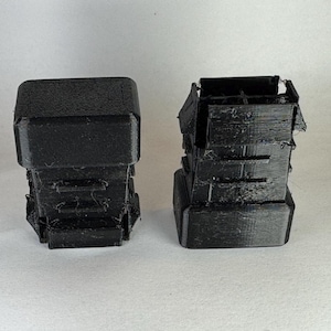May include: Two black 3D printed objects, one is a single block and the other is stacked blocks.