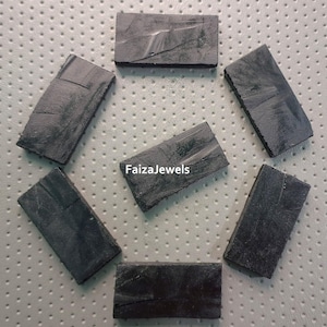 May include: Seven rectangular, dark grey stones arranged in a circular pattern. Each stone has a textured surface with visible lines and colour variations. The stones appear natural, possibly for jewellery or crafts.