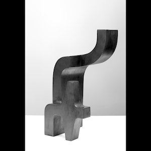 May include: Abstract sculpture made of black metal. The sculpture is composed of two interlocking forms, one of which is a long, curved shape that rises up and over the other.