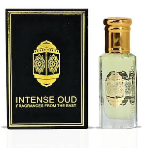 May include: A black box with gold lettering that reads "INTENSE OUD FRAGRANCES FROM THE EAST". The box contains a small, clear glass bottle with a gold cap and a light yellow liquid inside. The bottle has a gold label with an intricate design.