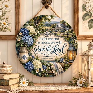 May include: A round wooden wall sign featuring a landscape with a house, blue and white hydrangeas, a pitcher, and a lantern. The text reads: As for me and my house, we will serve the Lord, JOSHUA 24:15. The sign hangs from a rope on a wall hook.