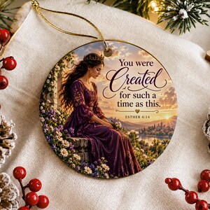 Könnte beinhalten: Ein rundes Keramikornament mit einer Frau in einem violetten Kleid, die bei Sonnenuntergang in einem Garten sitzt. Der Text lautet: You were Created for such a time as this. ESTHER 4:14. Das Ornament hat eine goldene Aufhängeschnur und eine glatte Oberfläche.