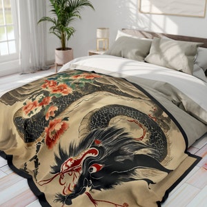 Può includere: Una coperta beige con un designo di drago giapponese nero e rosso. Il drago è circondato da fiori rosa e foglie verdi. La coperta è su un letto con cuscini bianchi e grigi.