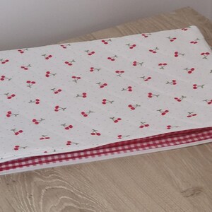 A white quilt with a red and white checkered pattern is placed on a wooden surface.