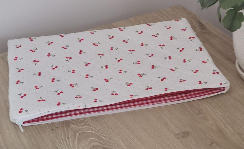 A white quilt with a red and white checkered pattern is placed on a wooden surface.