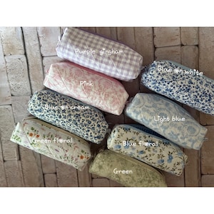 Puede incluir: Ocho estuches rectangulares acolchados con varios patrones que incluyen cuadros vichy morados, toile rosa, floral azul sobre blanco, floral azul sobre crema, toile azul claro, floral verde, floral azul y verde liso con etiquetas.