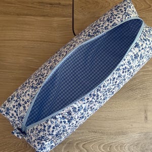 Könnte beinhalten: Ein rechteckiges, offenes Federmäppchen mit blauem Blumenmuster auf weißem Grund. Der Innenraum hat ein blau-weißes Vichy-Muster. Der Reißverschluss ist hellblau. Das Etui liegt auf einer Holzoberfläche.