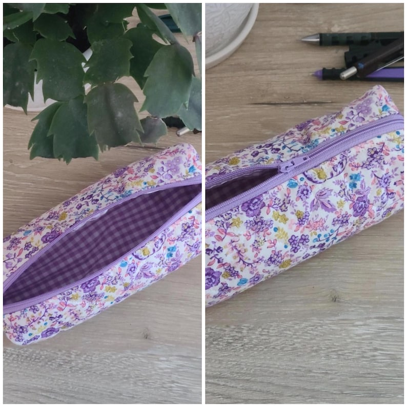 Puede incluir: Un estuche cil&iacute;ndrico con un estampado floral de flores moradas, rosas y amarillas sobre un fondo blanco. El estuche tiene una cremallera morada y un forro interior de tela con cuadros vichy en tonos morados y blancos.
