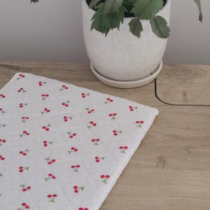 a white ceramic pot with a plant, a white cloth with red cherries, and a wooden surface.