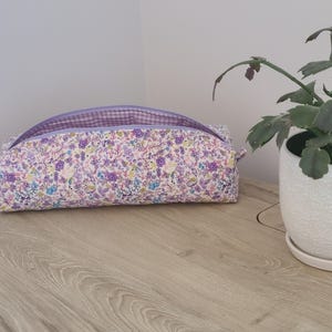 A floral patterned bag with a purple zipper sits on a wooden surface next to a potted plant.