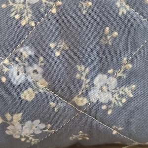 a close-up view of a fabric with a floral pattern, featuring small white flowers and leaves.
