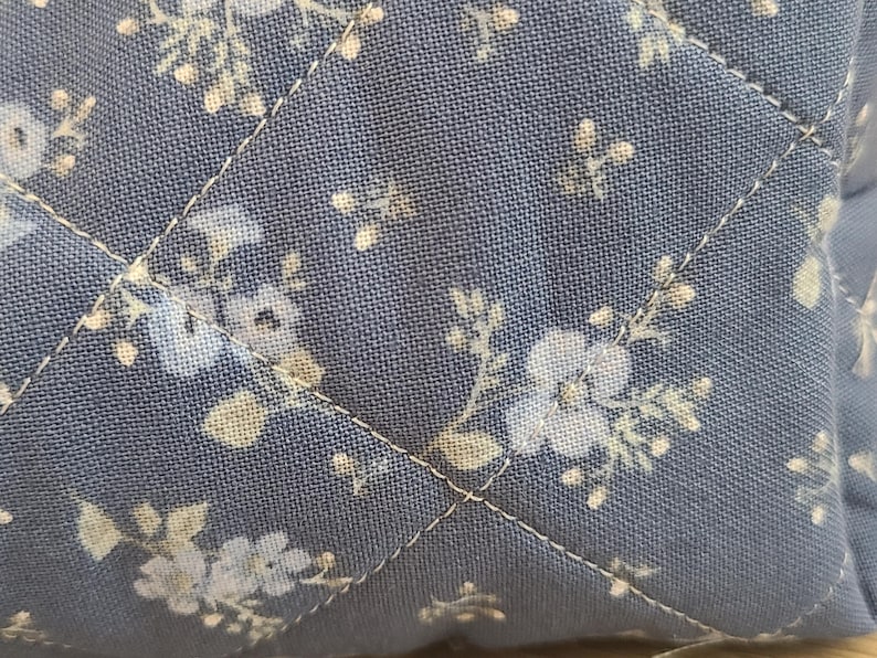a close-up view of a fabric with a floral pattern, featuring small white flowers and leaves.