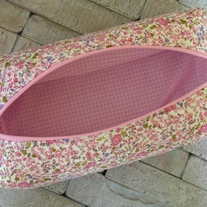May include: A rectangular zippered pouch featuring a floral pattern with pink, yellow, and purple flowers on a cream background. The interior is lined with a pink and white gingham fabric. A pink zipper runs along the top opening of the pouch.