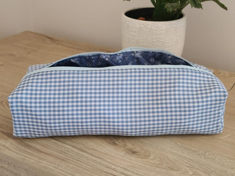 A blue and white checkered bag is placed on a wooden surface, with a potted plant visible in the background.