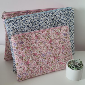 Pode incluir: Três bolsas acolchoadas retangulares com fecho de correr. A maior bolsa apresenta um padrão floral rosa, a do meio tem uma estampa floral azul e a bolsa frontal menor exibe um denso padrão floral rosa e verde.