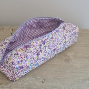 A purple and white floral patterned pencil case is open and resting on a wooden surface.