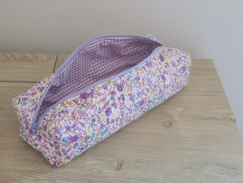 A purple and white floral patterned pencil case is open and resting on a wooden surface.