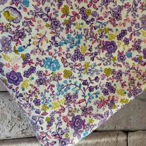 May include: A fabric featuring a dense floral pattern on a pale yellow background. The design consists of small purple roses, light blue blossoms, and tiny yellow flowers connected by thin, dark purple stems and delicate pink leaves throughout.