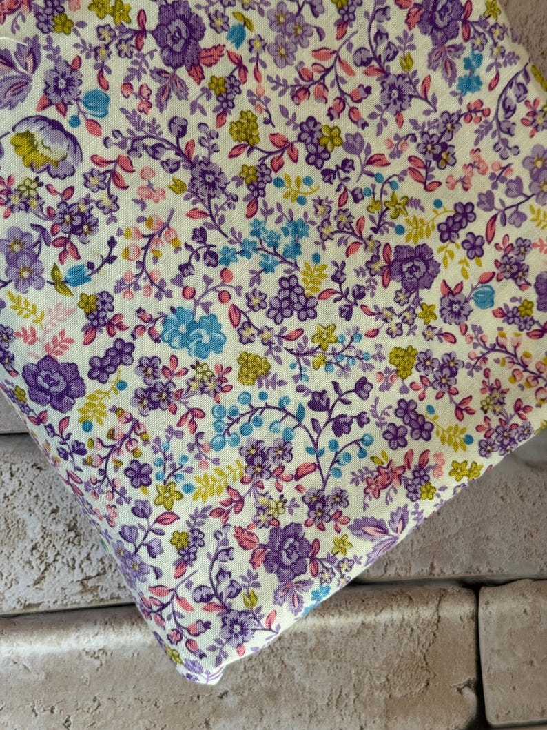 May include: A fabric featuring a dense floral pattern on a pale yellow background. The design consists of small purple roses, light blue blossoms, and tiny yellow flowers connected by thin, dark purple stems and delicate pink leaves throughout.