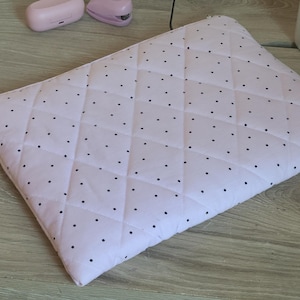 May include: A light pink quilted laptop sleeve featuring a diamond-stitched pattern with small black polka dots scattered across the fabric. The rectangular sleeve has a zippered closure along the top edge and a soft, padded construction for protection.